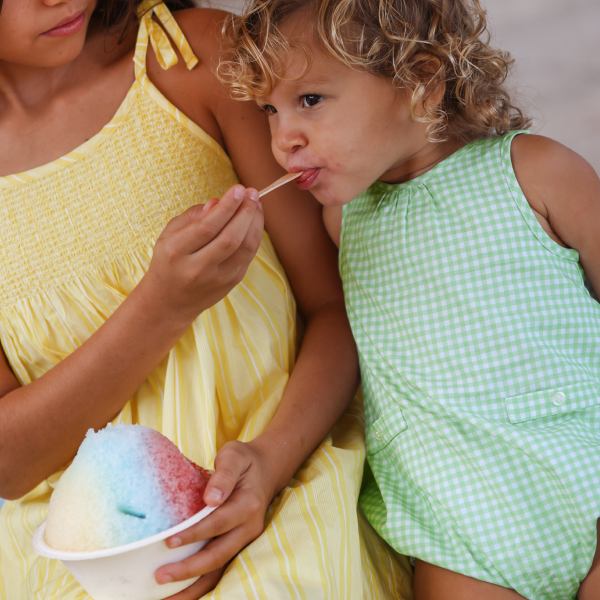 little girl wearing minnow romper eating a snowcone