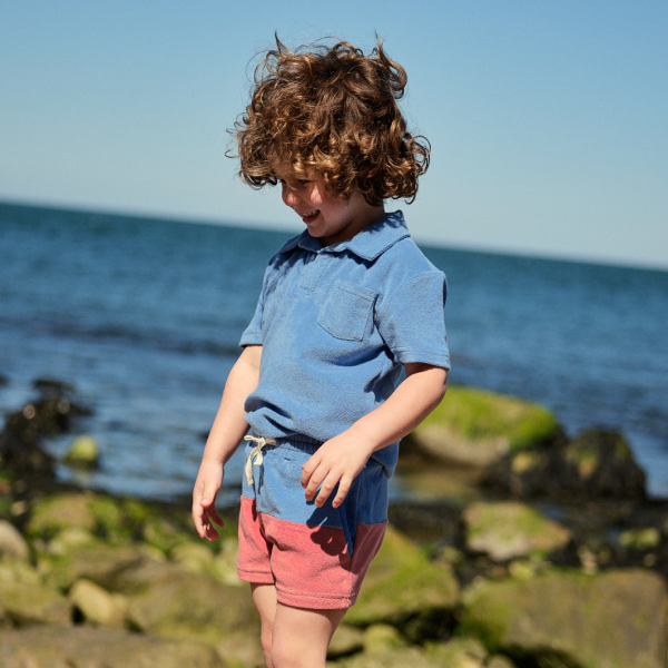 boy wearing minnow french terry polo and coordinating colorblock shorts on rocks near. beach